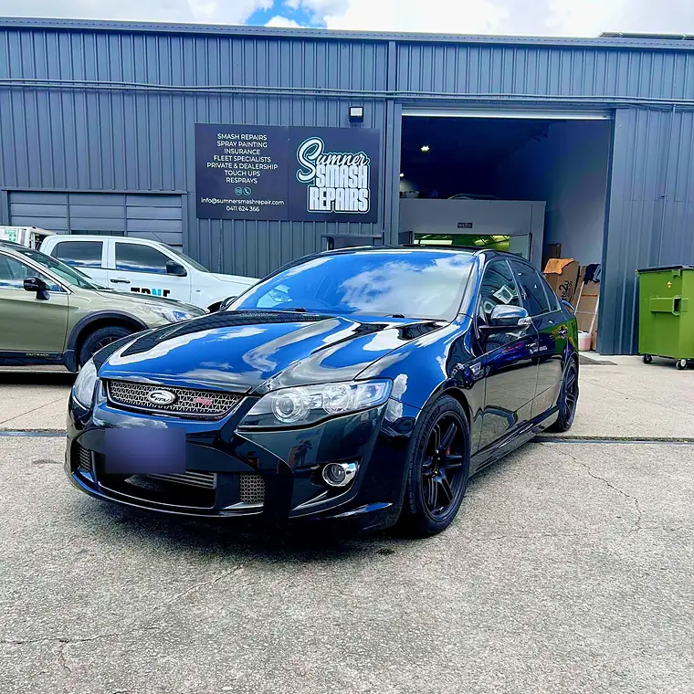 Black sedan with a gloss finish parked in front of the Sumner Smash Repairs sign at Unit 2