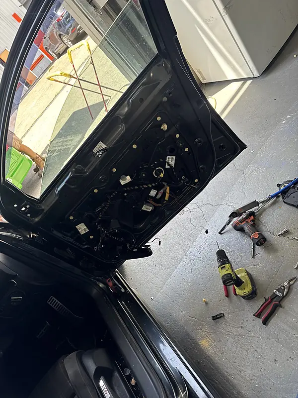 Car door with its trim panel removed and tools laid out on the workshop floor