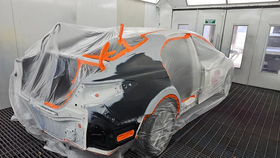 Car masked in plastic and orange tape inside the spray booth, ready for paint